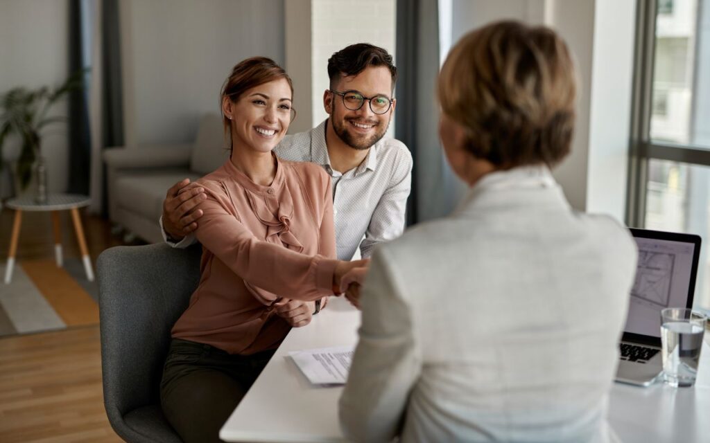 Casal jovem sorridente contratando seguro prestamista Sicredi com consultora financeira em escritório moderno