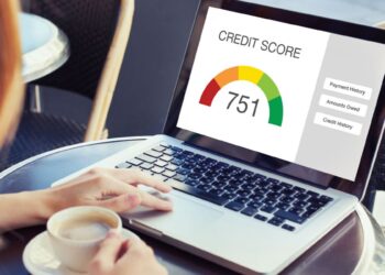 Mulher consulta score de crédito positivo (751) em laptop com xícara de café ao lado.
